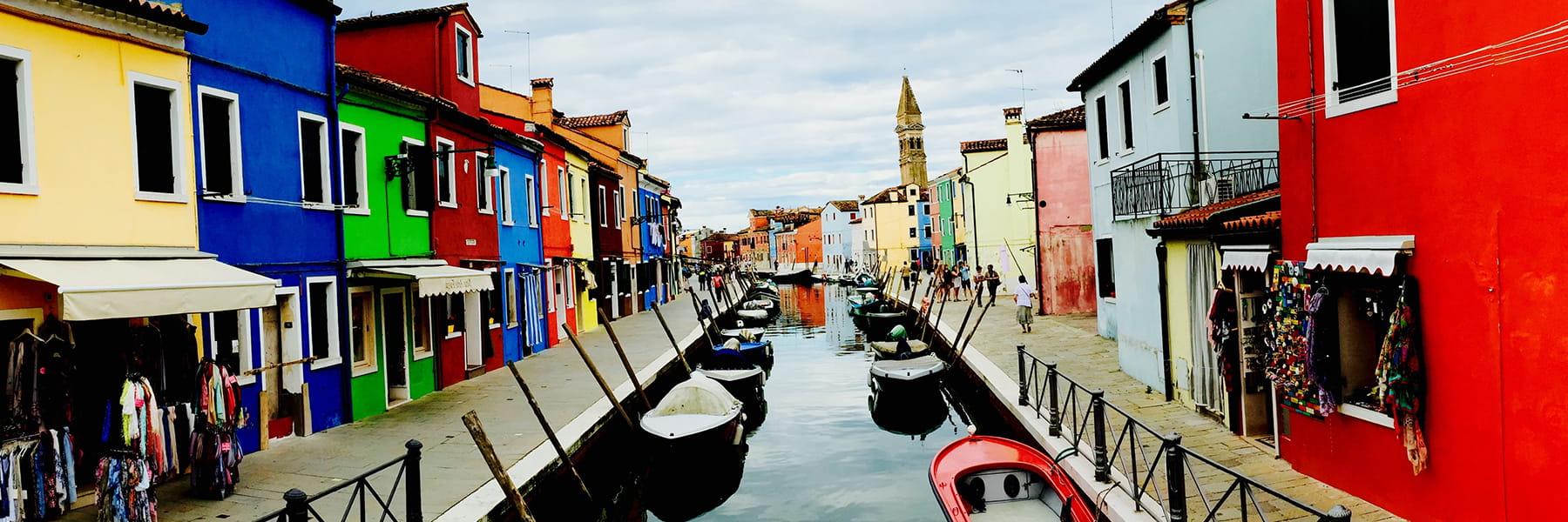 View of canals bordered by houses and boats docked to sides.